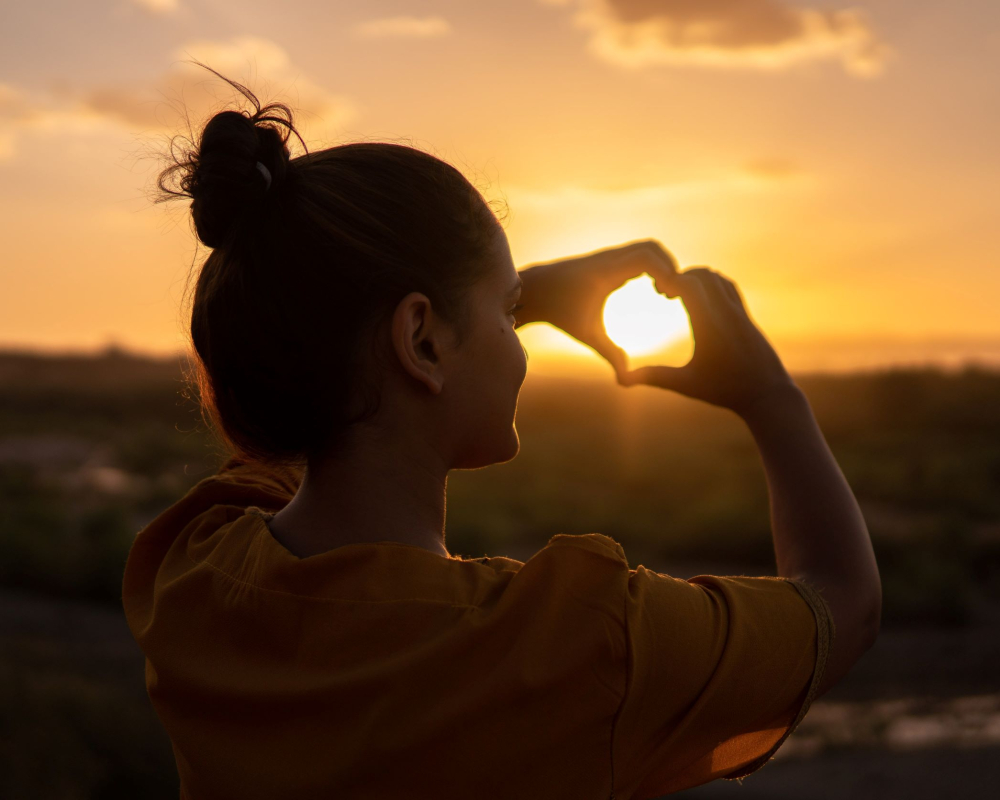 A woman is doing a heart sign towards the sign.
