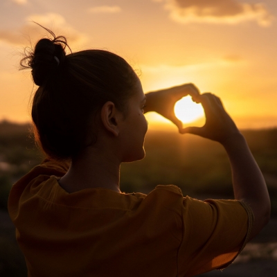 A woman is doing a heart sign towards the sign.